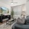 Spacious and well lit living room with wood flooring, large windows and open access to the kitchen